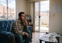Cómo ampliar una casa Infonavit pequeña sin gastar demasiado Propietario en la sala de su casa Infonavit pequeña planea cómo ampliarla, con un plano en la pared y una cinta métrica sobre la mesa